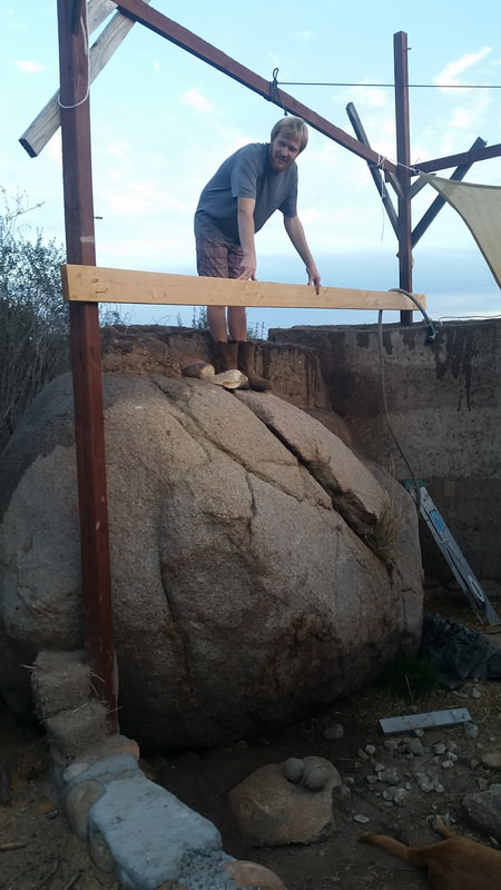 Chris Meador of Permasystems standing on large boulder where cob house walls are built of off