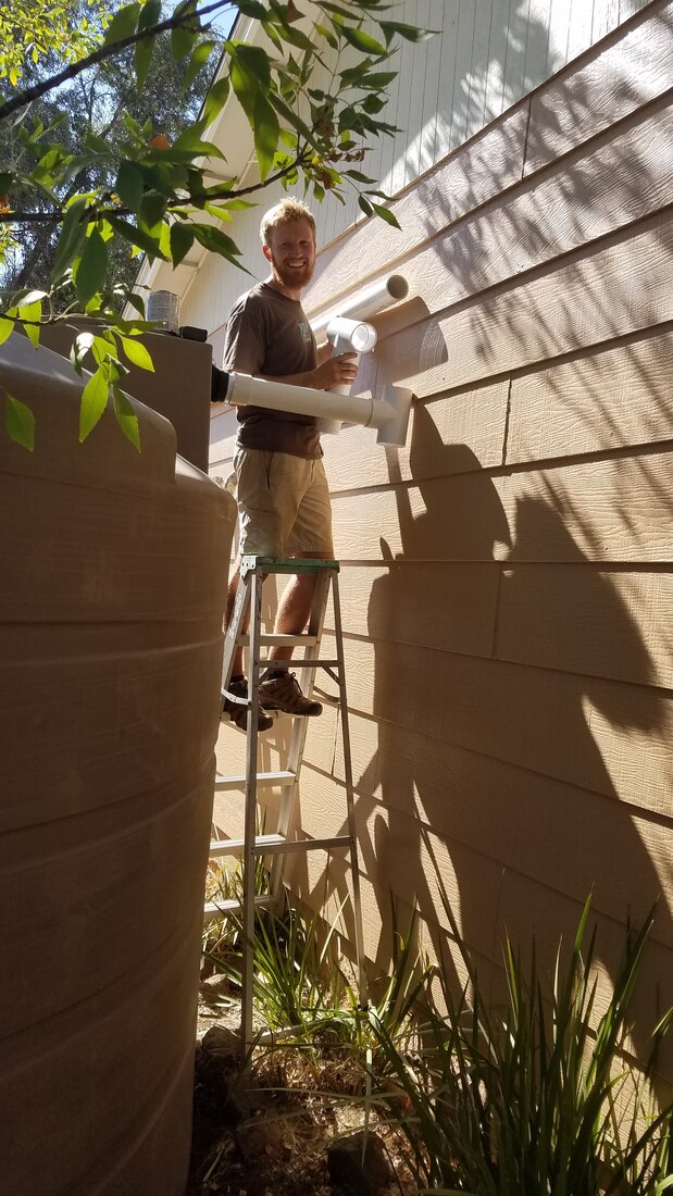 Chris Meador of Permasystems installing a rainwater harvesting system on ladder next to large water tank about to glue pipes in Ramona, San Diego County
