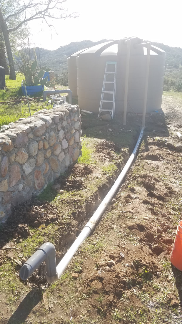 Two 5000 gallon rainwater harvesting tank with pipe coming out of one for overflow running to a drain