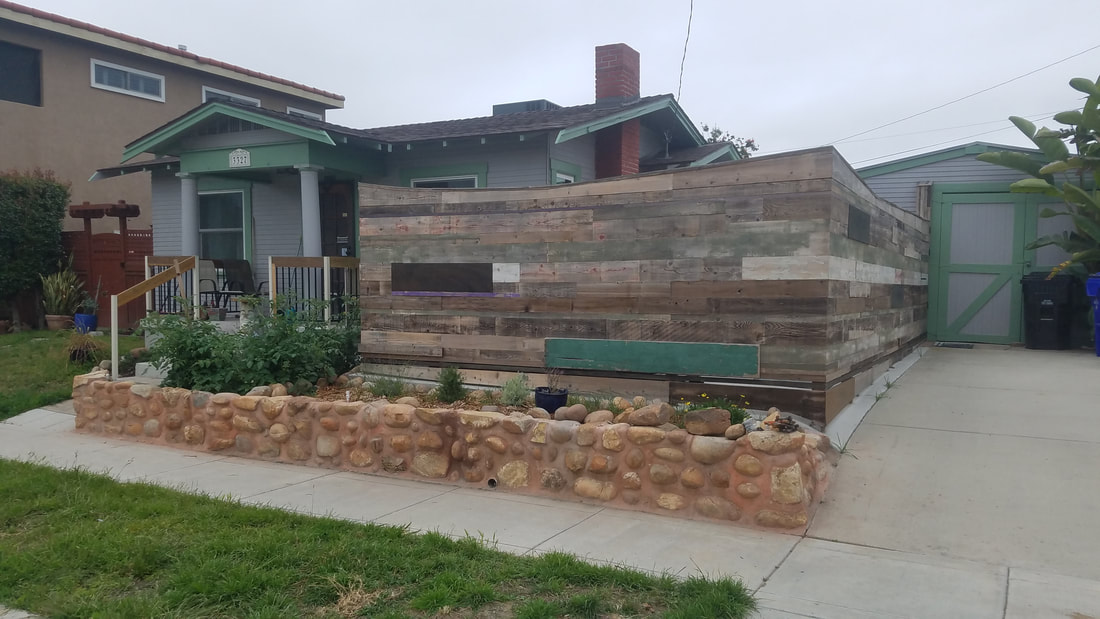 Home with 2 foot tall round rock retaining wall in front next sidewalk and fence using reclaimed wood behind the wall in Normal Heights, San Diego