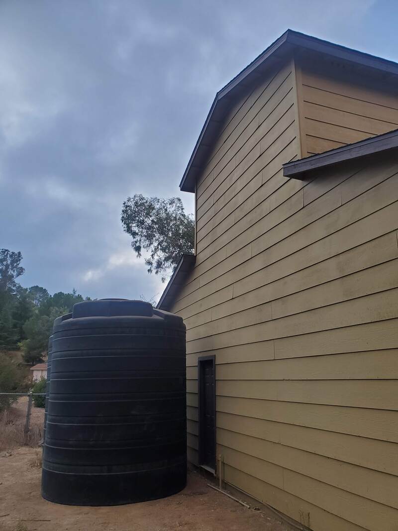 4050 gallon green Bushman water tank next to barn collecting water from roof in Ramona, CA