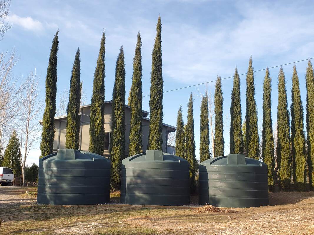 Three dark green five thousand gallon Bushman rainwater harvesting tanks attached to barn for collection in Julian, San Diego County, California
