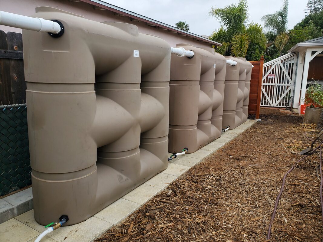 Three tan 530 gallong Bushman Slimline rainwater harvesting tank daisy chained alone fenceline in San Diego