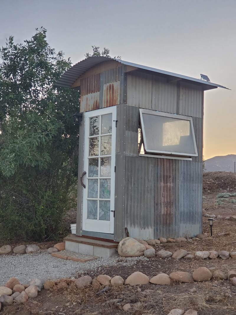 A small shack serves as a compost toliet system built using reclaimed doors, windows and corrugated metal siding
