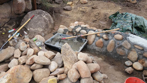 Rock and cement wall about 1 foot high in progress to be the stem wall for an earthen cob home in San Diego County